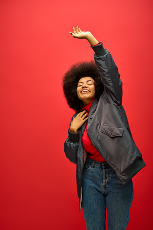 Stylish African American woman poses in trendy attire against a bold red backdrop.の写真素材