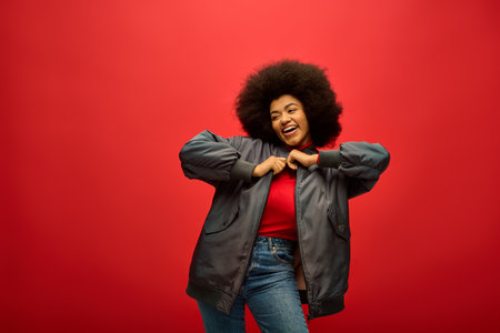 Stylish African American woman with curly hairdohair standing confidently against a striking red background.の写真素材