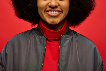 Close-up of African American woman smiling in trendy jacket against vibrant backdrop.の写真素材