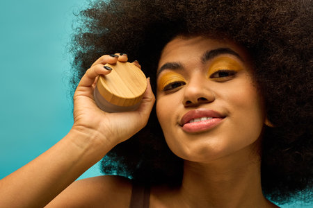 Stylish African American woman holding cream to face in trendy attire on vibrant backdrop.