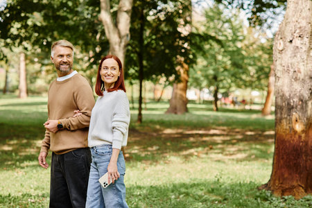 A man and a woman in casual attire stand side by side in a lush park.の写真素材