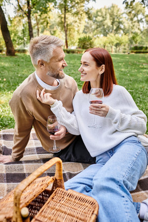 A man and woman sit on a blanket in a park, holding wine glasses.の写真素材