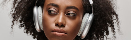 A beautiful young African American woman with curly hair wearing headphones over her face, immersed...