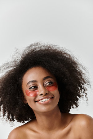 A beautiful young African American woman with curly hair showcasing eye patches in a studio setting.の写真素材
