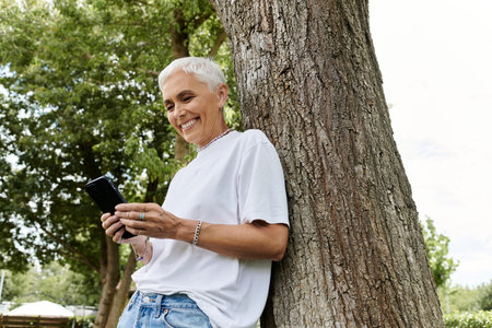 A mature woman smiles while texting, enjoying the outdoors and sunshine.