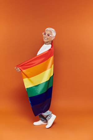 Mature woman joyfully showcases pride with a rainbow flag wrapped around her.の写真素材
