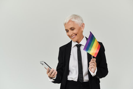 A confident woman joyfully engages with her phone, proudly holding a rainbow flag.の写真素材