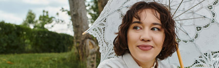 A cheerful young woman relaxes in summer, savoring a picnic while sheltered under a lace umbrella.の写真素材