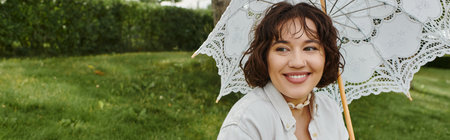 A young woman relaxes under a lace parasol, enjoying a sunny summer day in a lush green setting.の写真素材