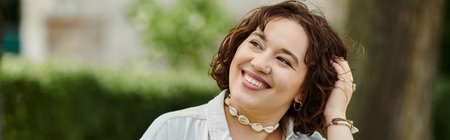 A cheerful young woman relaxes and smiles, basking in the warm sunshine of a green park during summer.の写真素材