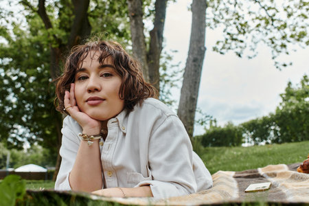 A young woman rests peacefully on a picnic blanket, savoring a sunny summer day in nature.