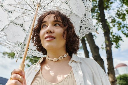 A young woman with curly hair smiles while relaxing in a lush park on a sunny summer day.の写真素材