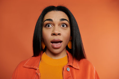 A young woman shows a look of surprise in a vibrant orange setting.の写真素材