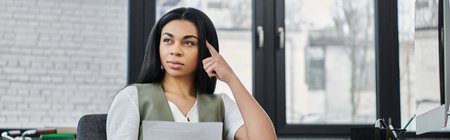 A thoughtful woman reflects while seated in a bright workspace.