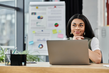 A thoughtful woman reflects while working at her desk in a vibrant workspace.の写真素材