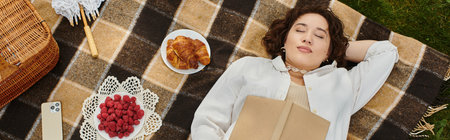 A young woman in a white shirt relaxes on a picnic blanket, savoring a summer day filled with berries and pastries.の写真素材