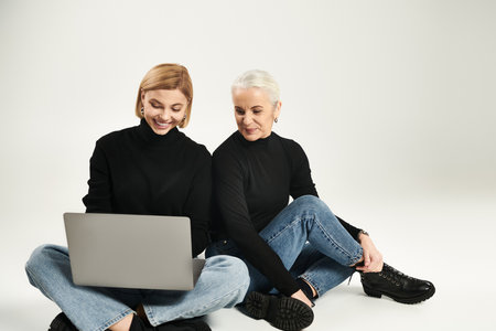 A woman and her daughter share a joyful moment, engaging with a laptop together.の写真素材