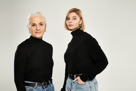 A mature woman stands gracefully beside her adult daughter, both styled elegantly.