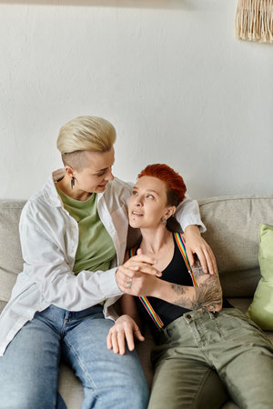 Two women, a lesbian couple with short hair, are cozily sitting together on a couch at home.の写真素材