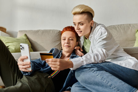 Two women, a lesbian couple with short hair, sit on the floor at home, discussing financial matters while holding a credit card.の写真素材