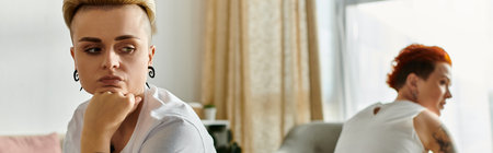 A lesbian couple with short hair sit in a room, facing each other, sharing a deep moment of...