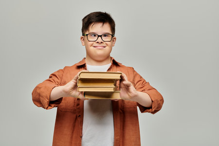 A boy with Down syndrome happily holds a stack of books on a gray background.の写真素材