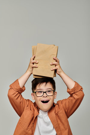 Cute child with Down syndrome playfully holding stack of books.の写真素材