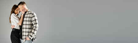 A man and woman, young and in love, stand together in a studio with a grey background, sharing a...