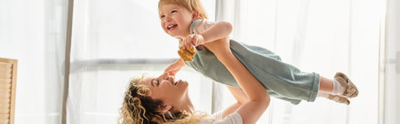 A curly mother lovingly holds her toddler daughter in her arms at home.の写真素材