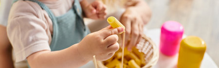 A curly-haired toddler joyfully plays with dry pasta, exploring textures and shapes in a Montessori-inspired learning moment.の写真素材