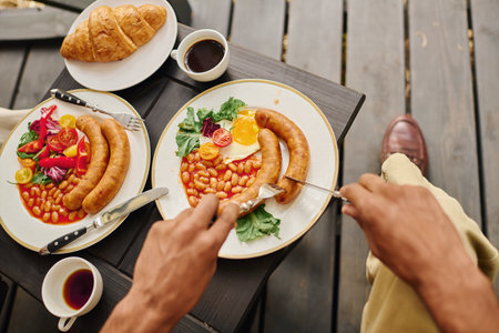 man enjoys a lunch, delicately cutting into a plate of delicious food with knife and fork.の写真素材