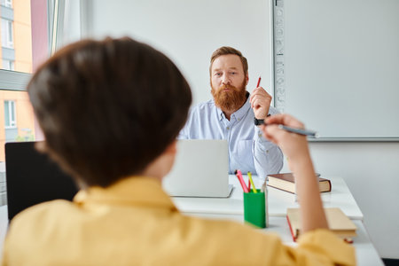 A bearded man sits at a desk, engaged in thought, possibly preparing a lesson or researching.の写真素材