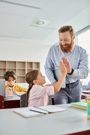A man stands beside a little girl in a vibrant classroom, engaging in a learning activity with a...