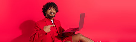 Young Indian man in red jacket holds laptop.の写真素材