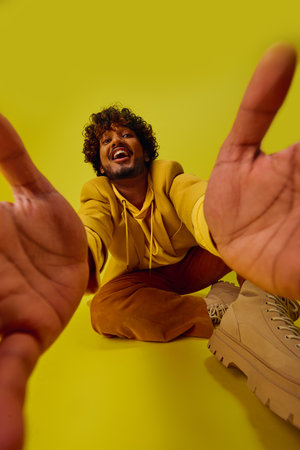 A man in a vibrant outfit sitting on the ground with his hands raised in the air.