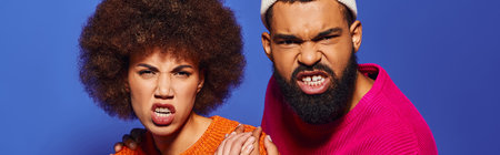 A young African American man and woman in vibrant attire, expressing emotions on a blue background.の写真素材