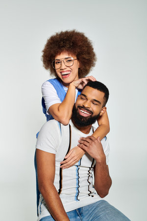 An African American man holds a woman on his shoulders, showcasing strength and friendship in...