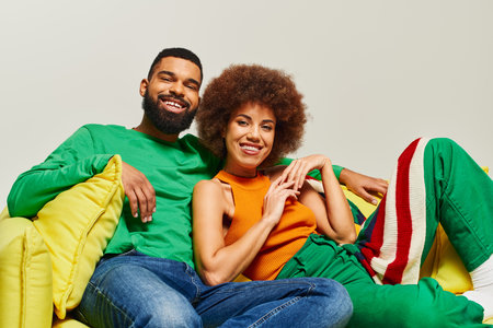 Happy African American friends in vibrant clothes sitting on a yellow bean bag chair, exuding warmth...