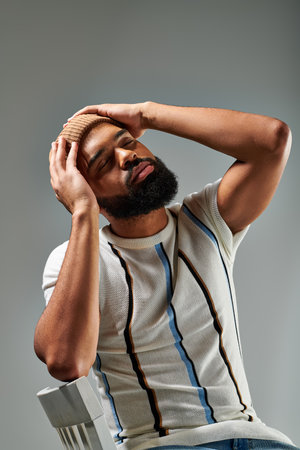 A stylishly dressed African American man with a beard sitting comfortably in a chair against a grey background.の写真素材
