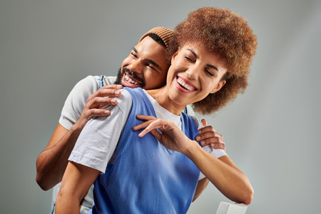 African American friends in stylish clothes hugging each other, showcasing friendship and connection on a grey background.の写真素材