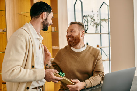 A man warmly presents a gift to another man in a store, their smiles reflecting the shared love and affection.の写真素材