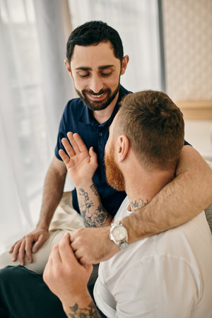 Two men with arm tattoos sitting on a bed, enjoying each others company in a modern living room.の写真素材