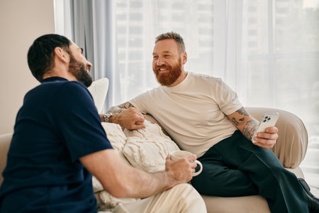 Two men in casual clothes, a happy gay couple, sit on a couch in a modern living room, engaging in a lively conversation.の写真素材