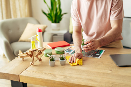 A man in cozy homewear sitting at a table cleaning near laptop.の写真素材