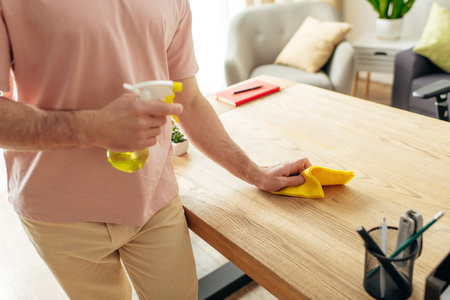 Handsome man in cozy homewear cleaning a table with a yellow cloth.の写真素材