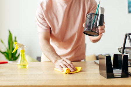 A suave man in cozy attire cleans a table with a sponge.の写真素材