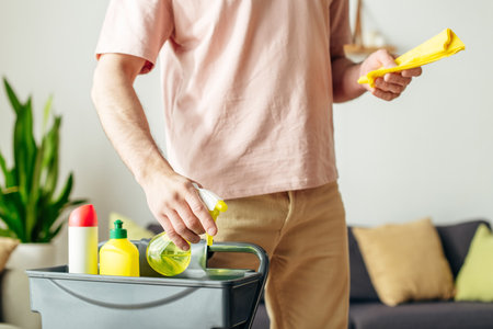 A man in cozy homewear cleans a living room with a yellow sprays.の写真素材