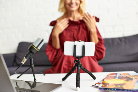 Mature woman in red dress records podcast on beauty from laptop.