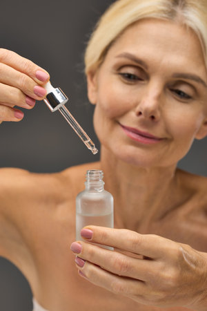 Charming mature woman applying serum on a gray backdrop.の写真素材