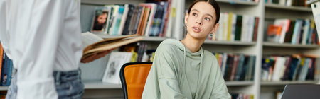 A tutor with red hair teaches a teenage girl at a desk in a library, using a laptop for modern...